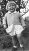 Lorraine Moll, about 3, standing in front of a bush